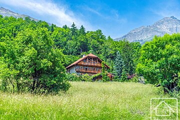 A wooden chalet nestled in a vibrant green mountain landscape with a grassy field under a clear blue sky.