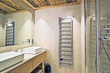 Modern bathroom with wooden plank ceiling, twin white vessel sinks on a light wood vanity, a chrome towel warmer, and a glass shower.