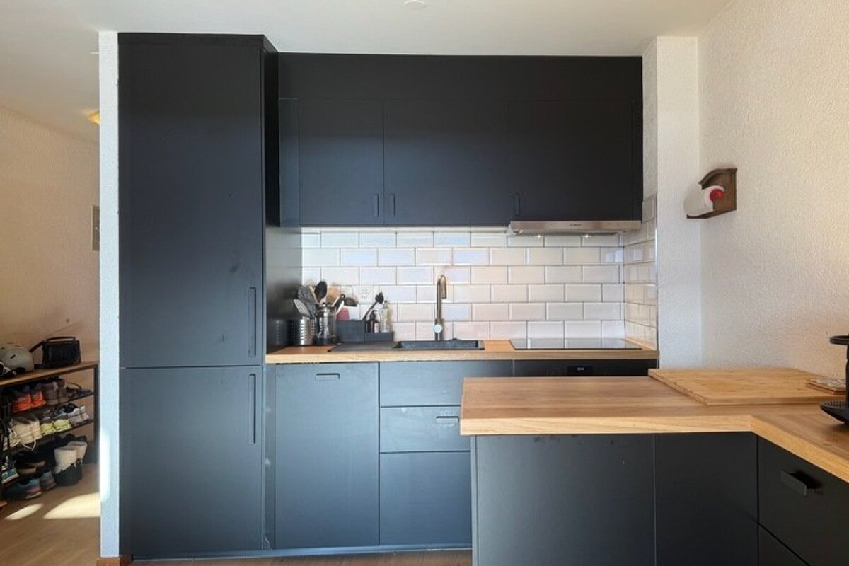 Modern kitchen featuring matte black cabinets, wooden countertops, and a white subway tile backsplash.