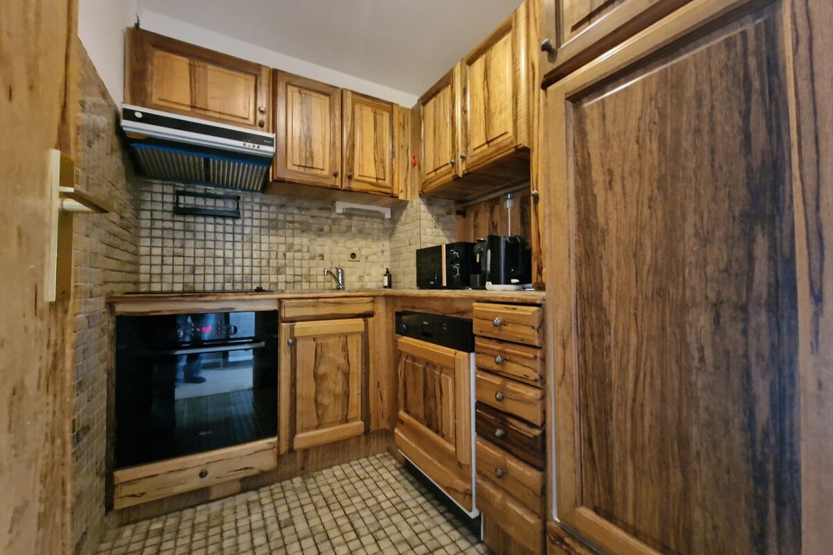 Compact kitchen with varied-grain wooden cabinets, light tiled backsplash and floor. Includes an oven, microwave, and coffee maker.