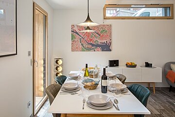 Modern dining room featuring a set white table, colorful chairs, a hanging lamp, and city map artwork on the wall.