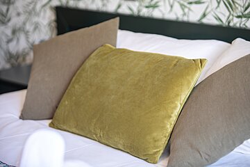 A yellow pillow sits on a bed with other pillows