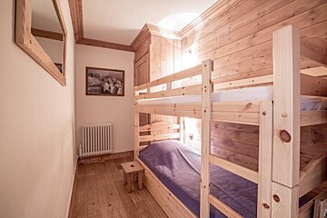 A cozy wooden cabin bedroom featuring light pine bunk beds, wood-paneled walls, and a hardwood floor.