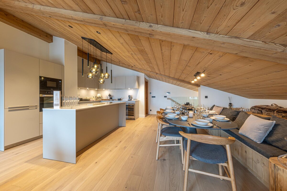 Modern open-plan kitchen and dining area with light wood floors, an impressive wooden ceiling, a set table, and built-in bench seating.