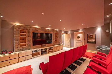 A luxurious home cinema room featuring rows of red recliner seats, a large screen, and a stylish stone wall with integrated wooden cabinetry.