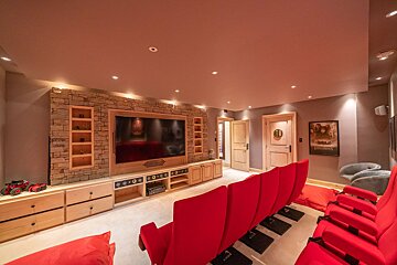 A cozy home theater featuring rows of bright red seats facing a large screen mounted on a rustic stone-accented entertainment center.