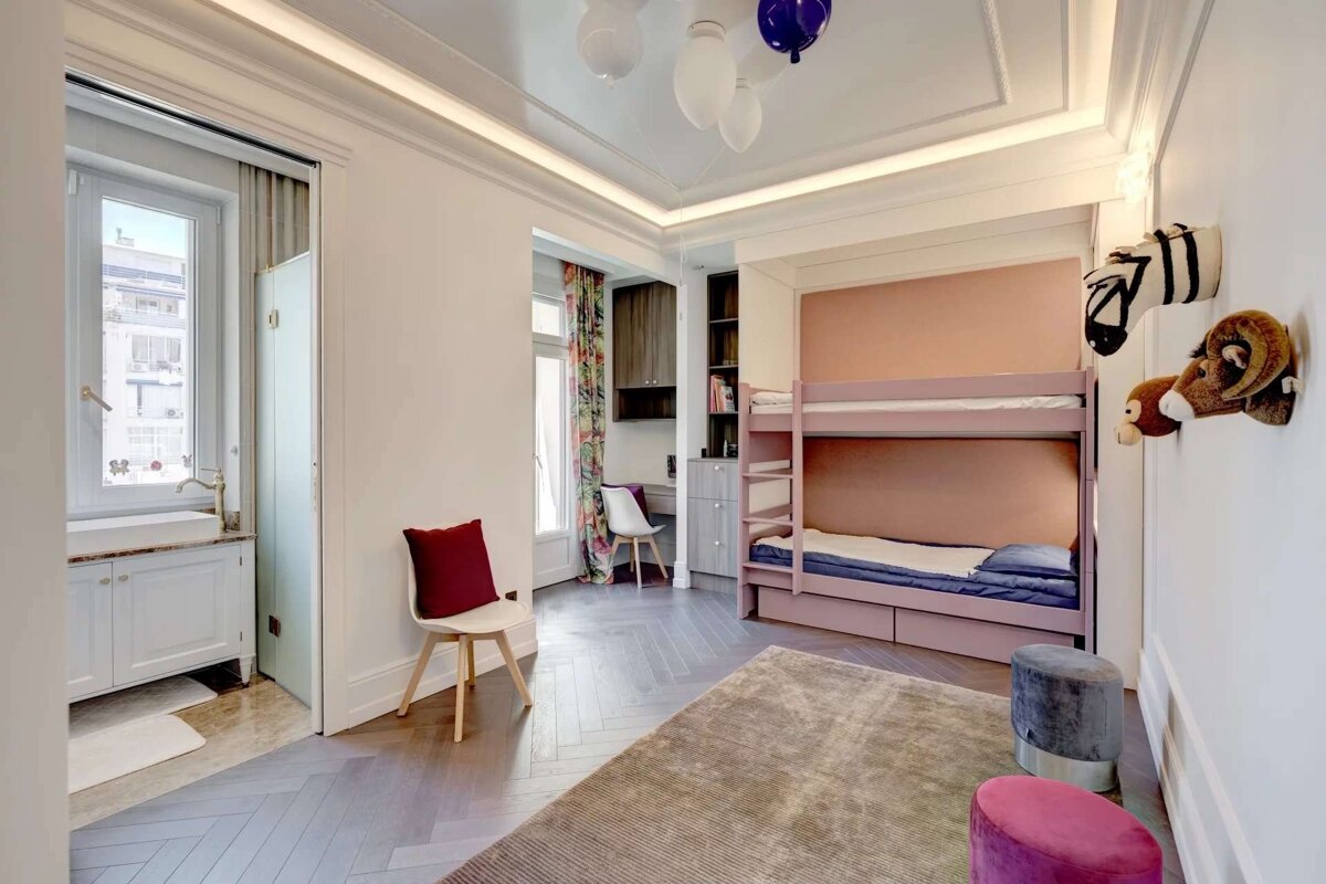 Modern kids' room with pink bunk beds, a desk nook, sink vanity by a window, playful animal wall decor, and balloon ceiling lights.