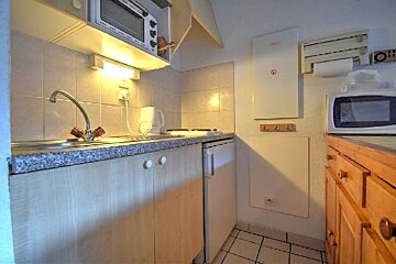 A compact kitchen with a sink, microwave, mini-fridge, and stove, featuring light wood cabinets and a granite-look countertop.
