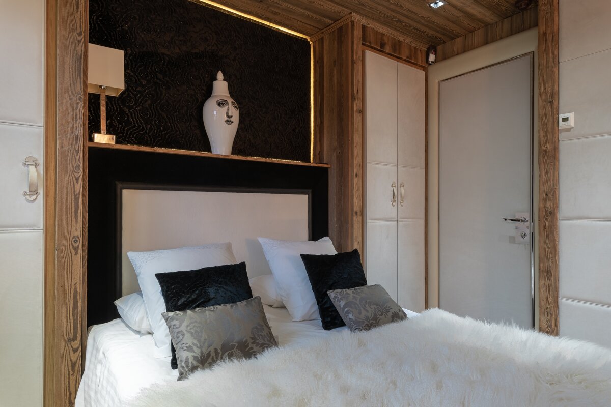 A cozy modern bedroom featuring a fluffy white bed, a dark headboard with a unique face vase, warm wooden paneling, and built-in storage.