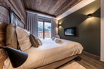 Cozy chalet bedroom with wood paneling, an olive green wall, and a balcony overlooking snowy mountains.