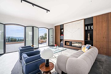 Bright, modern living room with arched glass doors revealing a scenic view. Features a sleek fireplace, built-in shelves, and contemporary decor.
