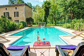 A bottle of wine sits on a table next to a swimming pool