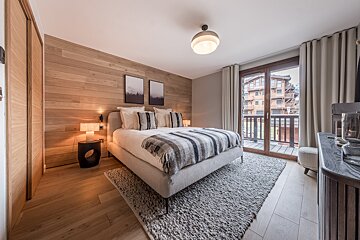 Warm, modern bedroom with wood plank wall, cozy bed, large window to a balcony, and textured rug.