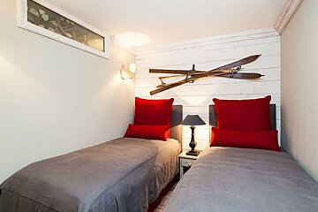 Cozy twin bedroom with red pillows, grey bedding, and vintage wooden skis on a white shiplap wall, creating a rustic lodge feel.
