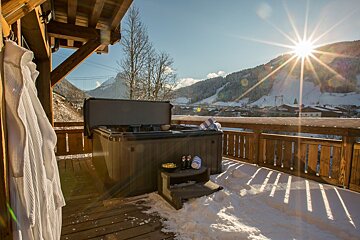 A hot tub sits on a snowy deck with a mountain in the background