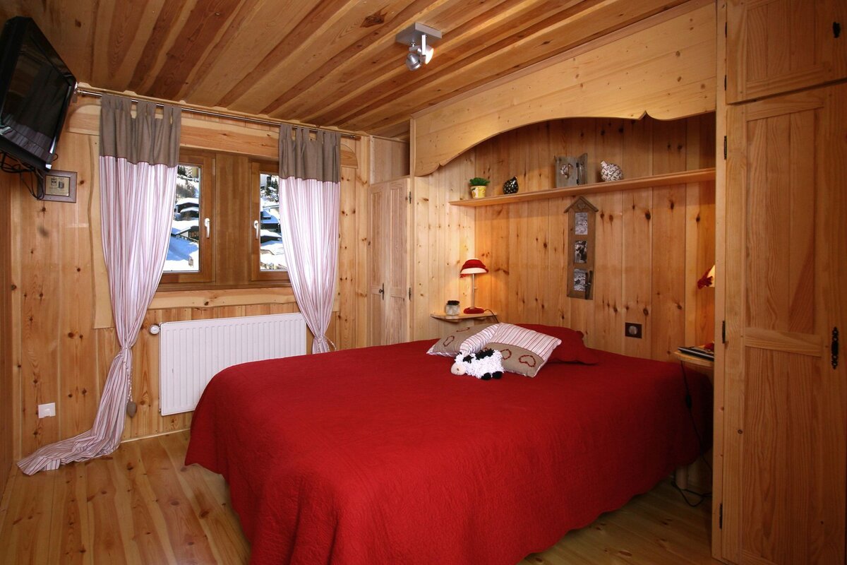 A bedroom with a red bed and a sheep pillow