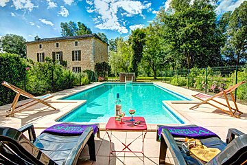 A bottle of wine sits on a table in front of a swimming pool