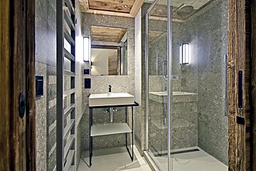 Modern stone-tiled bathroom featuring a glass walk-in shower, a minimalist sink on a black stand, and rustic wooden accents.