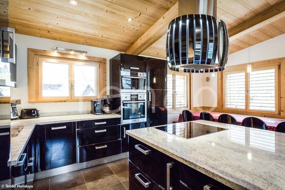 Modern kitchen with glossy black cabinets, granite countertops, a wooden ceiling, and a unique cylindrical range hood over the island.