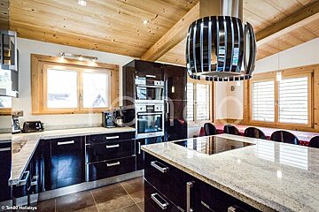Modern kitchen with glossy black cabinets, granite countertops, a wooden ceiling, and a unique cylindrical range hood over the island.