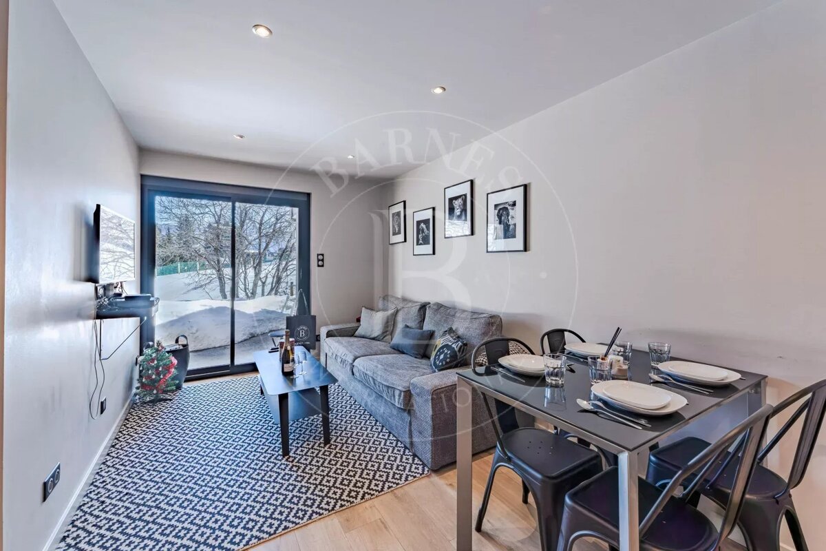 Modern living room with a grey sofa, dining area, and a large sliding door revealing a snowy outdoor scene. Features a black and white patterned rug.