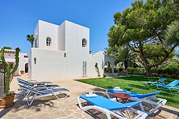 A white house with blue lounge chairs in front of it