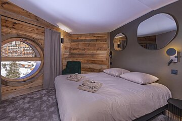 A bedroom with a round window and two mirrors