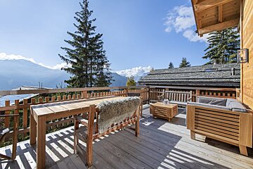 A wooden deck with a table and chairs with mountains in the background