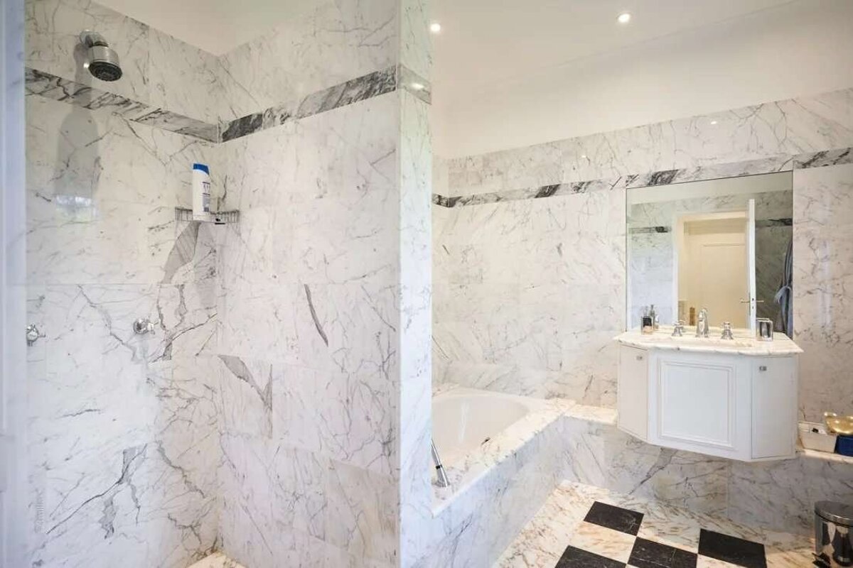 Elegant bathroom with white/grey marble walls, a black/white checkered floor, shower, tub, and vanity.