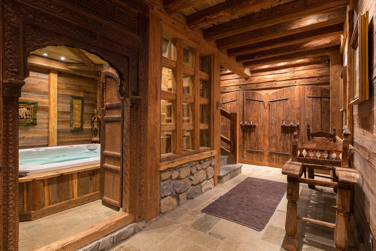 Rustic wooden interior featuring a carved archway leading to a jacuzzi area, with a stone-floored hallway and antique wooden details.