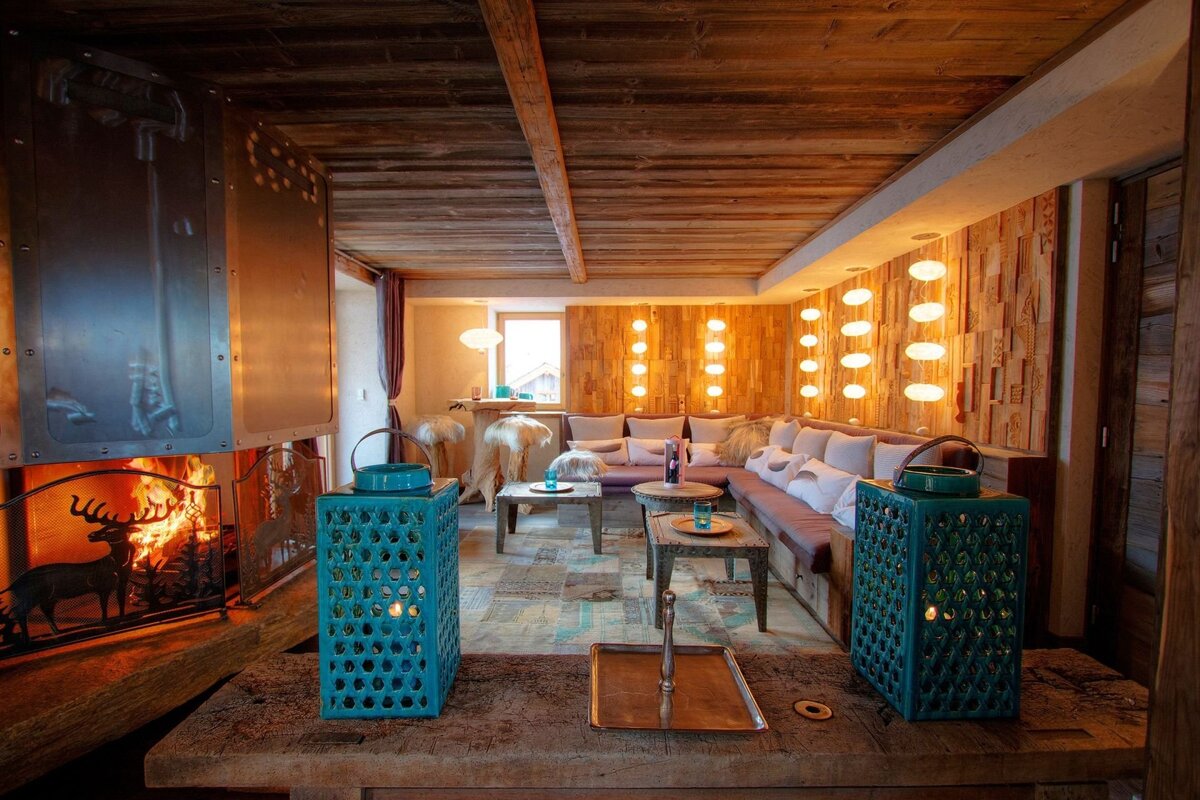 Cozy, rustic lounge with a burning fireplace, wooden walls, ambient lighting, comfortable seating, and decorative lanterns.