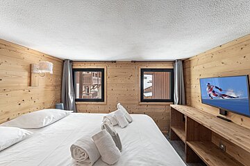 A bedroom with a large bed and a flat screen tv showing a person skiing