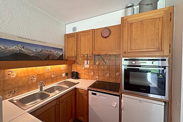 Cozy kitchen with wooden cabinets, a double sink, integrated appliances, and a panoramic mountain picture above the counter.
