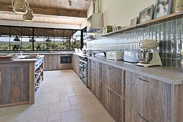 Rustic kitchen featuring natural wood cabinetry, a large window overlooking a scenic landscape, modern appliances, and a stylish tiled backsplash.