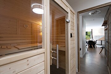 A wooden sauna with a glass door leading to a dining room