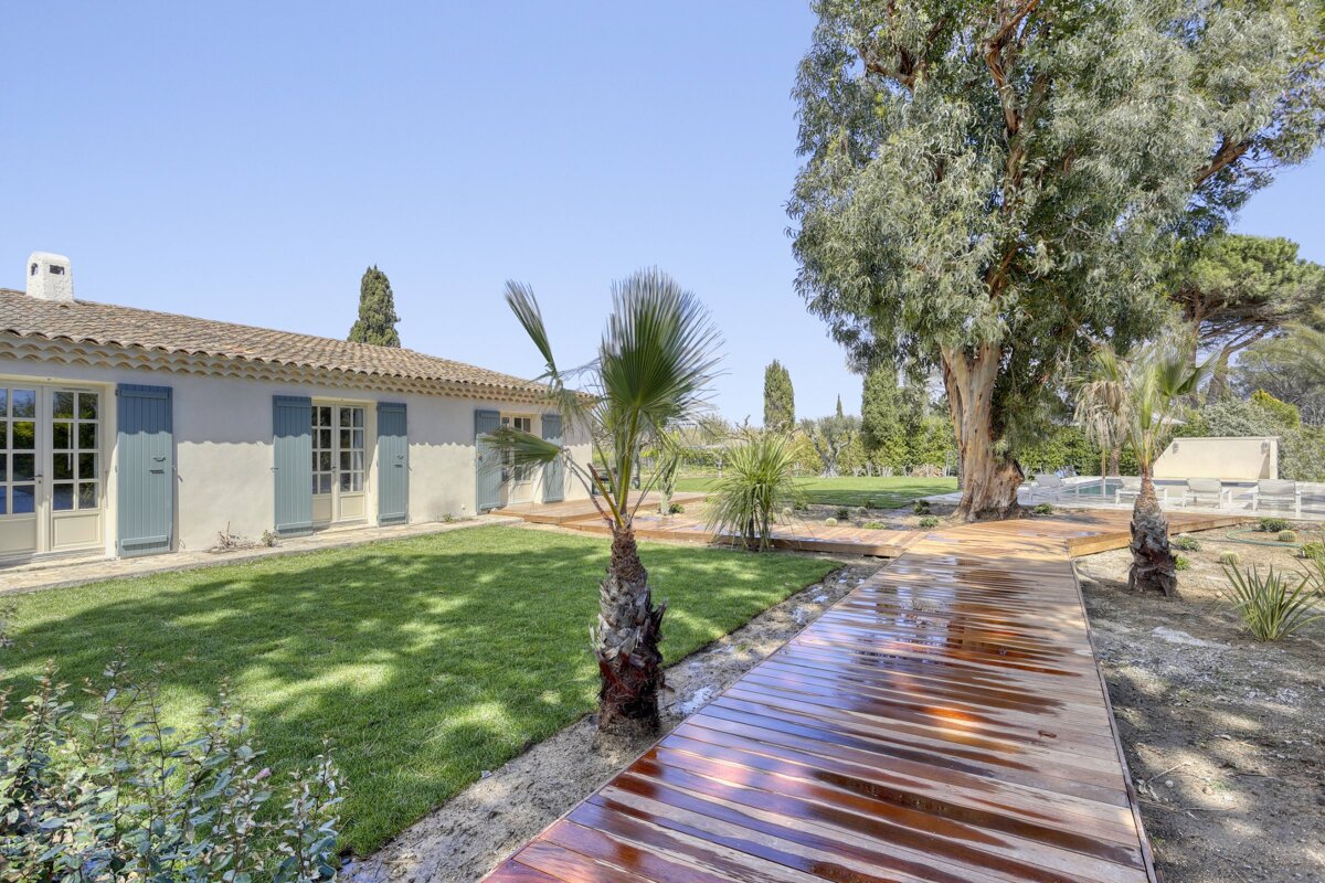 A wooden walkway leads to a white house with blue shutters