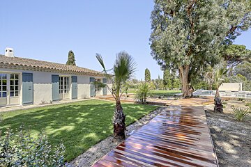 A wooden walkway leads to a white house with blue shutters