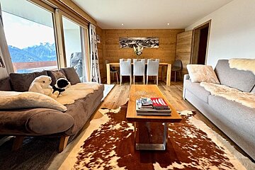 Cozy chalet living room featuring two sofas, a cowhide rug, a wooden coffee table, and a dining area in the background.