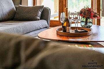 Champagne, flutes, and a floral arrangement on a wooden coffee table next to a grey sofa.
