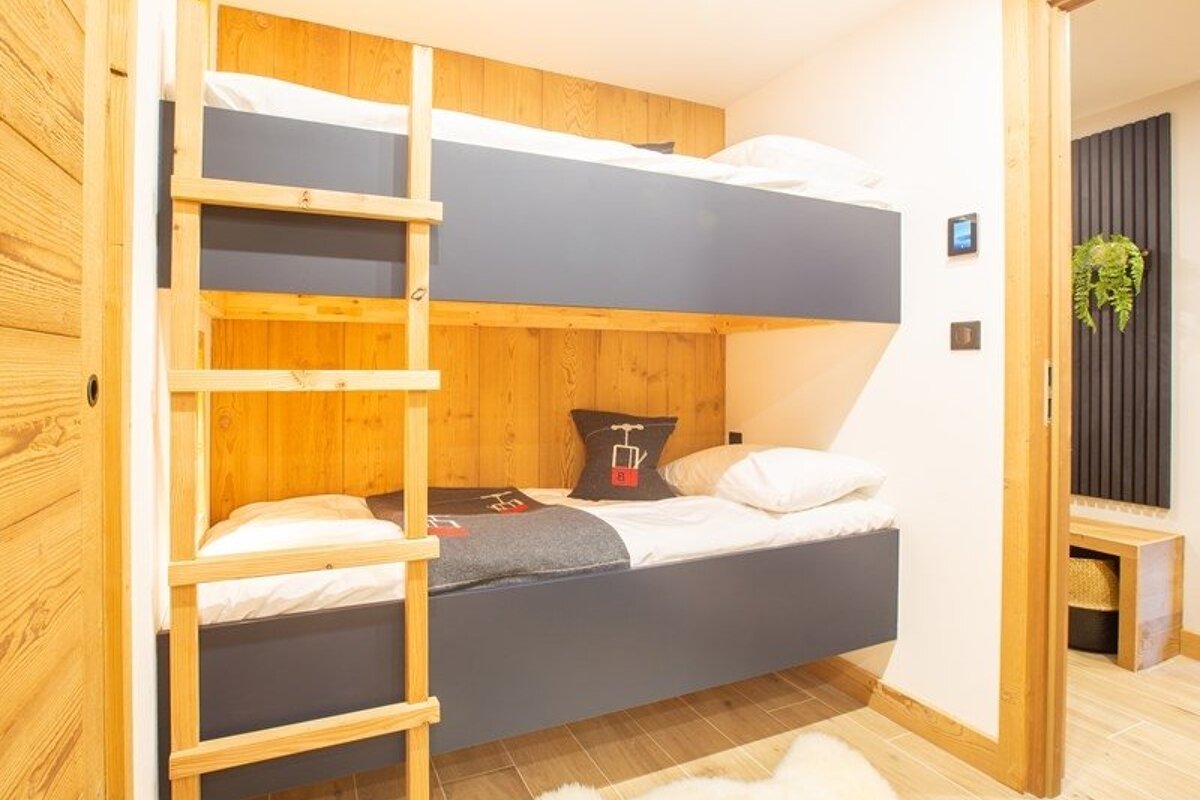 Cozy cabin bedroom featuring a wooden bunk bed with dark grey panels, a ladder, and warm wood walls.
