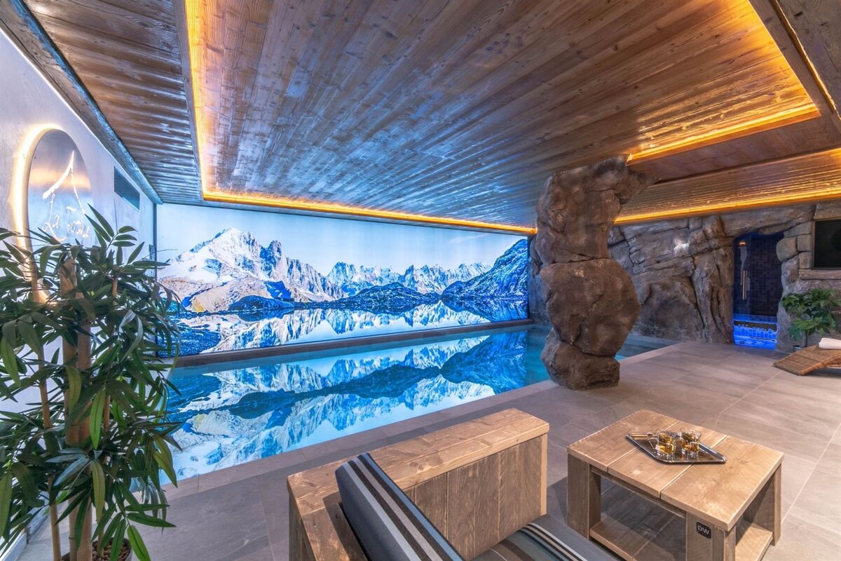 Luxurious indoor pool with a scenic mountain backdrop reflecting in the water, a wooden ceiling, and natural rock features.