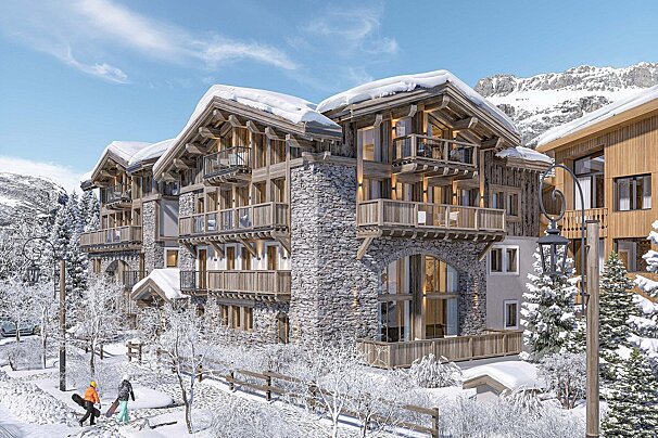 Luxurious stone and wood chalets blanketed in snow, set against a mountainous backdrop. Two people carry snowboards through the winter wonderland.