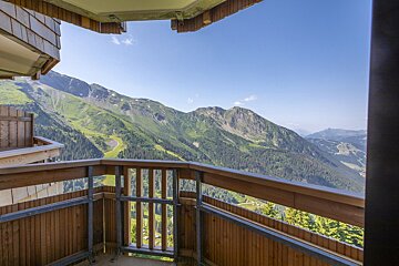 View from a wooden balcony overlooking lush green mountains, dense forests, and distant valleys under a clear blue sky.