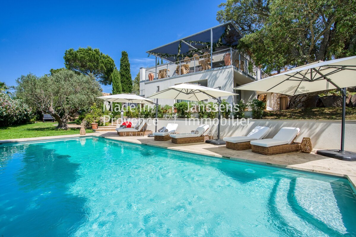 A large swimming pool is surrounded by chairs and umbrellas and is for sale by janssens immobilier