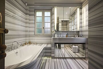 Luxurious bathroom with striped marble walls and floor, featuring a white tub, double sink vanity with mirrors, and a window.