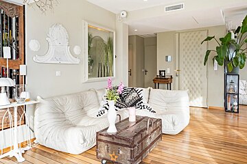 A modern living room with a white Togo sofa, a vintage trunk coffee table, light wood floors, and neutral walls.