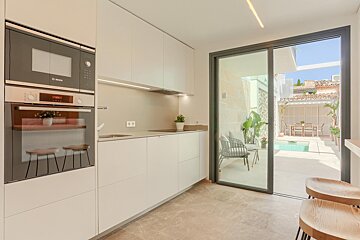 Modern white kitchen with built-in appliances, overlooking a sunlit patio featuring a swimming pool and outdoor seating.
