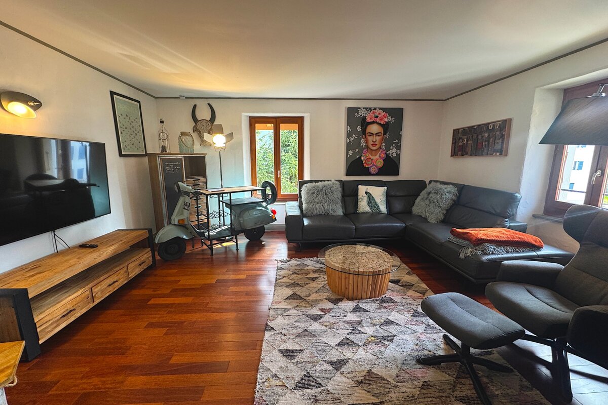 A stylish living room with a grey L-shaped sofa, TV, wooden floors, a geometric rug, a large Frida Kahlo painting, and a unique Vespa scooter bar.