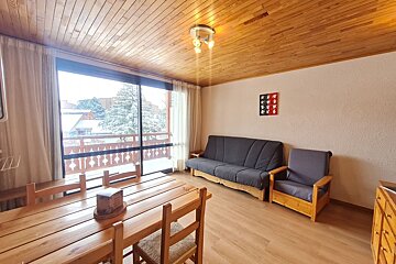 Cozy wooden cabin interior featuring a dining table, gray seating, and a large glass door showing a snowy view outside.