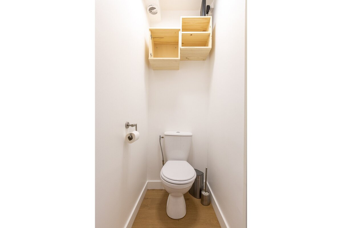 A toilet with a wooden shelf above it